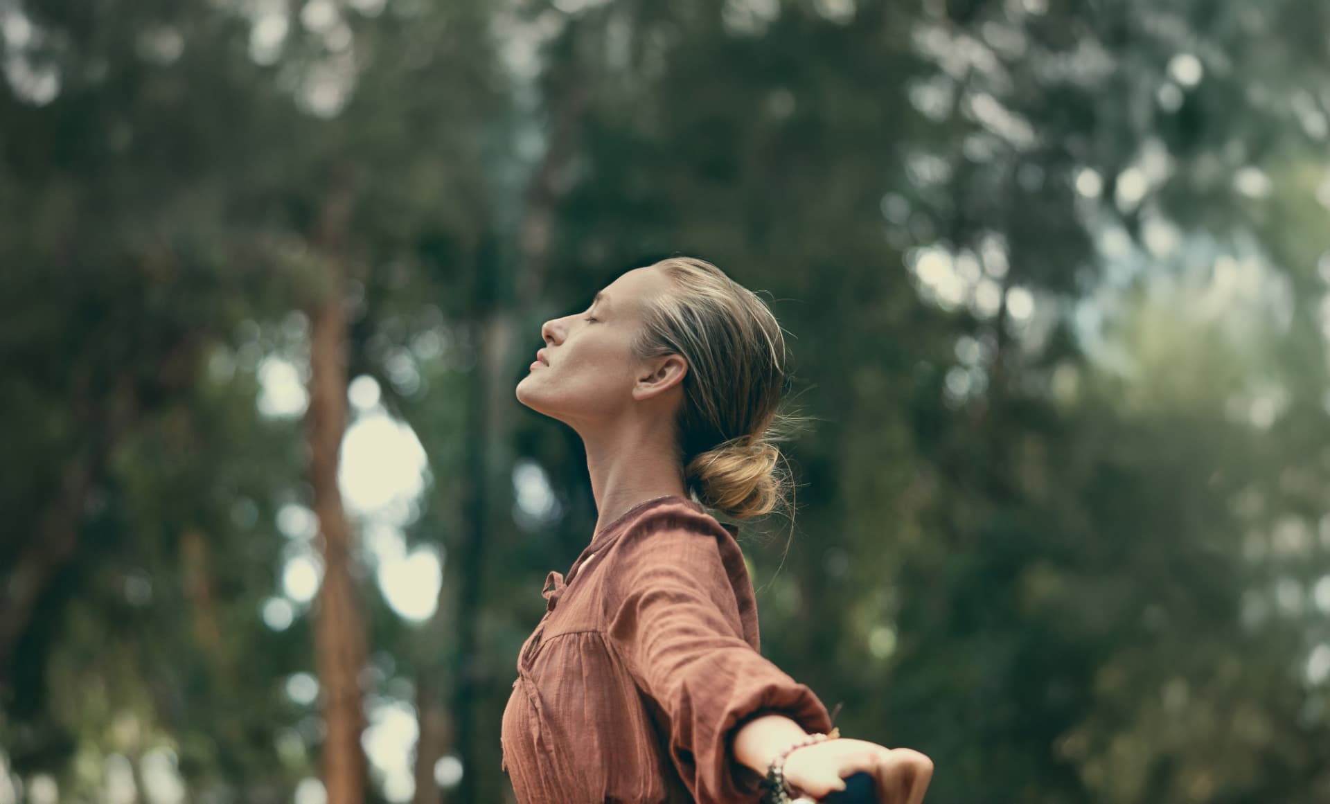 Woman walking with outstretched arms through a shaded garden